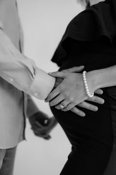 two people are holding hands while wearing pearls on their wrists in black and white