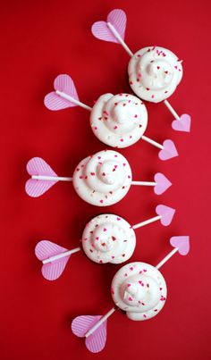 cupcakes with white frosting and pink sprinkles are arranged on a red surface