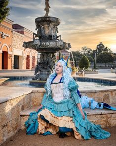 a woman dressed in blue and white sitting next to a fountain