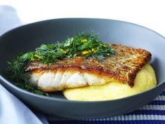 a fish fillet is served on top of grits in a gray bowl with green garnish