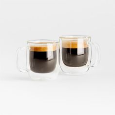 two cups of coffee sitting next to each other on a white surface with one cup filled with liquid