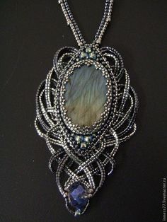 a necklace made with wire and glass beads on a black surface, featuring an oval shaped pendant