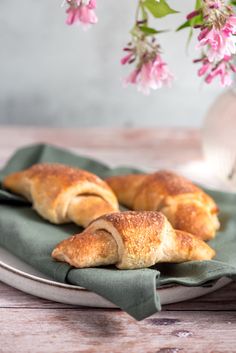 two croissants on a plate with pink flowers in the background