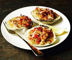 three cooked oysters on a plate with lemon wedges