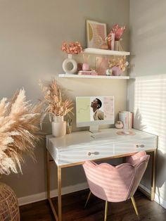 a desk with a computer and some flowers on it in front of a wall mounted shelf