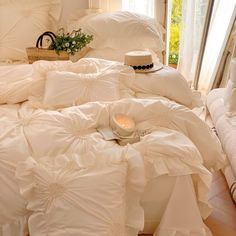 a bed with white comforters and pillows on top of it next to a window