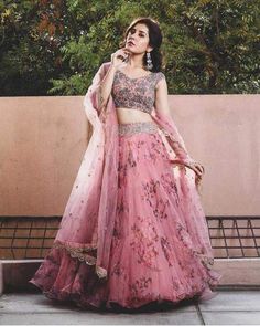 a woman in a pink lehenga and matching outfit poses for the camera with her hand on her hip