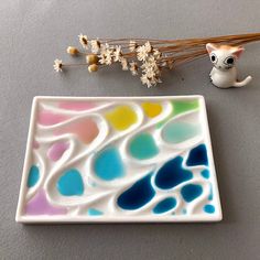 there is a small white plate with colorful designs on it and a cat figurine next to it