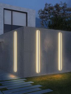 some lights that are on the side of a building in front of a grass field