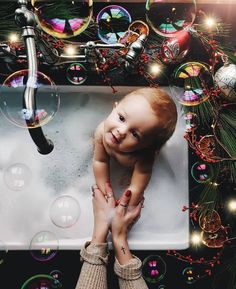 a baby sitting in a bathtub surrounded by soap bubbles and christmas decorations on the wall