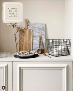 a white cabinet with utensils and wooden spoons on it, next to a black basket