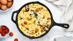 an omelet in a cast iron skillet with tomatoes and eggs around it