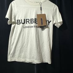 Burberry Black Shotover Logo T-Shirt Cotton T-Shirt Featuring Round Ribbed Collar, Contrasting Logo Lettering At The Front And Short Sleeves Very Hard To Get Now , Very Unusual With Logo Designer Letter Print Tops For Spring, Designer Spring Tops With Letter Print, Designer Tops With Letter Print For Spring, Designer Tan Crew Neck Top, Designer Tan Short Sleeve Top, Designer Short Sleeve Tan Top, Burberry Shirts, Burberry Tops, Burberry Black