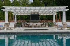 an outdoor kitchen and dining area next to a swimming pool with lounge chairs around it