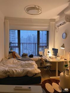 a bedroom with a bed, desk and television in it's corner area next to a large window