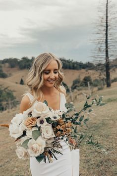 a woman holding a bouquet of flowers in her hand and smiling at the camera while standing on a hill