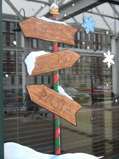 a pizza sign in front of a window with snow on the ground and buildings behind it