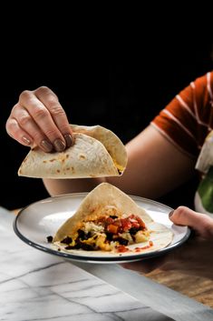 a person holding a tortilla over a plate with other food items on it