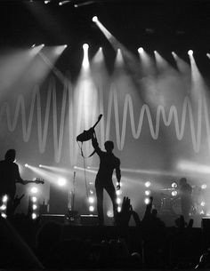 a man on stage with his arms in the air and lights behind him, holding a microphone