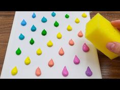 someone is using a sponge to make colorful raindrops on a white board with yellow paper