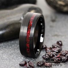 a wedding band with red and black inlays is shown next to some rocks