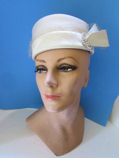 "Handsome vintage hat in winter white--the chance to wear white in the colder months.  The topper is in winter white felt with a 2\" brim of satin. To the left is a felt tab anchored by a 3 loop faux pearl and clear rhinestone decoration. A wide gauge net covers the brim. The 6\" across crown is welled. No maker label Size: label reads \"22\"--4\" tall; 21 1/2\" inner band circumference Condition: good vintage--body of hat is without stains or holes.  The interior band has slight evidence of mak Vintage White Costume Hat For Formal Occasions, Vintage White Formal Costume Hat, Cream Mini Hats For Vintage Events, White Vintage Cloche Fascinator, Vintage White Cloche Fascinator, White Adjustable Cloche Hat For Evening, Winter Wedding Cloche Mini Hat, White Fitted Retro Hat, Vintage White Brimmed Costume Hats And Headpieces