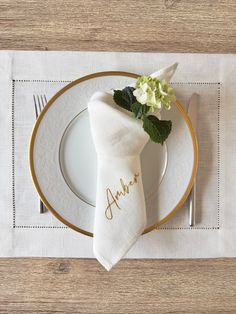 a place setting with white and gold plates, napkins, and flowers on it