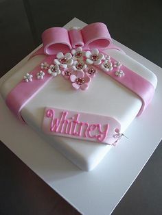 a white cake with pink ribbon and bow on top that says whitley's