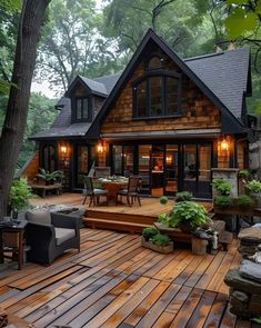 a wooden deck with chairs and tables in front of a cabin style house surrounded by trees