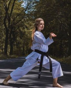 a young woman is practicing karate in the middle of the road with trees behind her