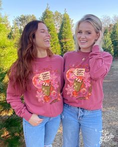 two young women standing next to each other in front of trees and smiling at the camera