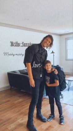 a man standing next to a little boy on top of a hard wood floor in front of a white wall