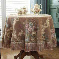 a table with a flowered tablecloth and two teapots sitting on top of it