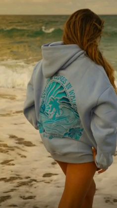 a woman is walking on the beach with her back to the camera and looking at the water