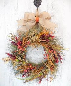 a wreath hanging on the side of a white wooden wall with an orange and brown bow