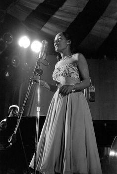 a black and white photo of a woman in a dress standing next to a microphone