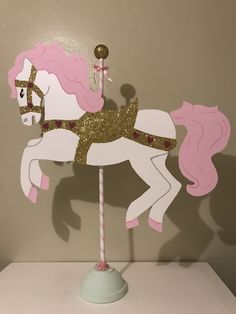 a pink and white carousel horse with glitter on it's head, standing in front of a wall