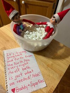 two elfs are sitting in a bowl with marshmallows on the table