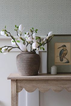 a vase filled with white flowers sitting on top of a wooden table next to a framed painting