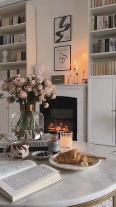 a table with flowers and books on it in front of a fire place filled with candles