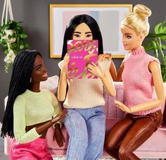 two barbie dolls are sitting on a couch and one is holding a pink heart shaped box