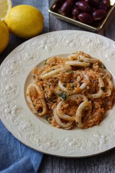 a white plate topped with pasta and olives next to a tray of lemons