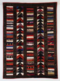 an old quilt hanging on the wall in front of a white wall with red and black stripes