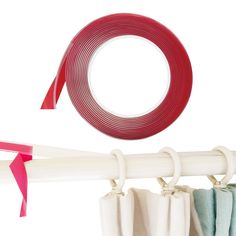 two rolls of red and white tape hanging from the side of a curtain rod with pink ribbon