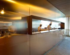 two chefs are preparing food in a large glass walled kitchen with stainless steel counter tops