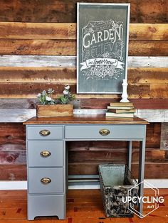 an old desk is painted blue and has some flowers on top of it in front of a wooden wall