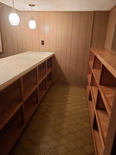 an empty room with wooden shelves and white counter tops in the corner, along with two hanging lights