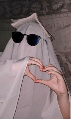 a person wearing sunglasses making a heart shape with their hands