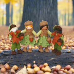 three little dolls are standing on a log in the woods with acorns all around them