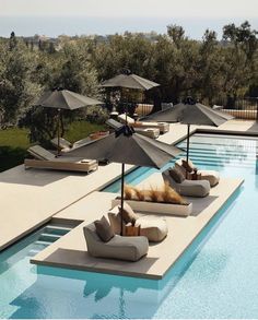 an outdoor swimming pool with lounge chairs and umbrellas on the side, surrounded by olive trees